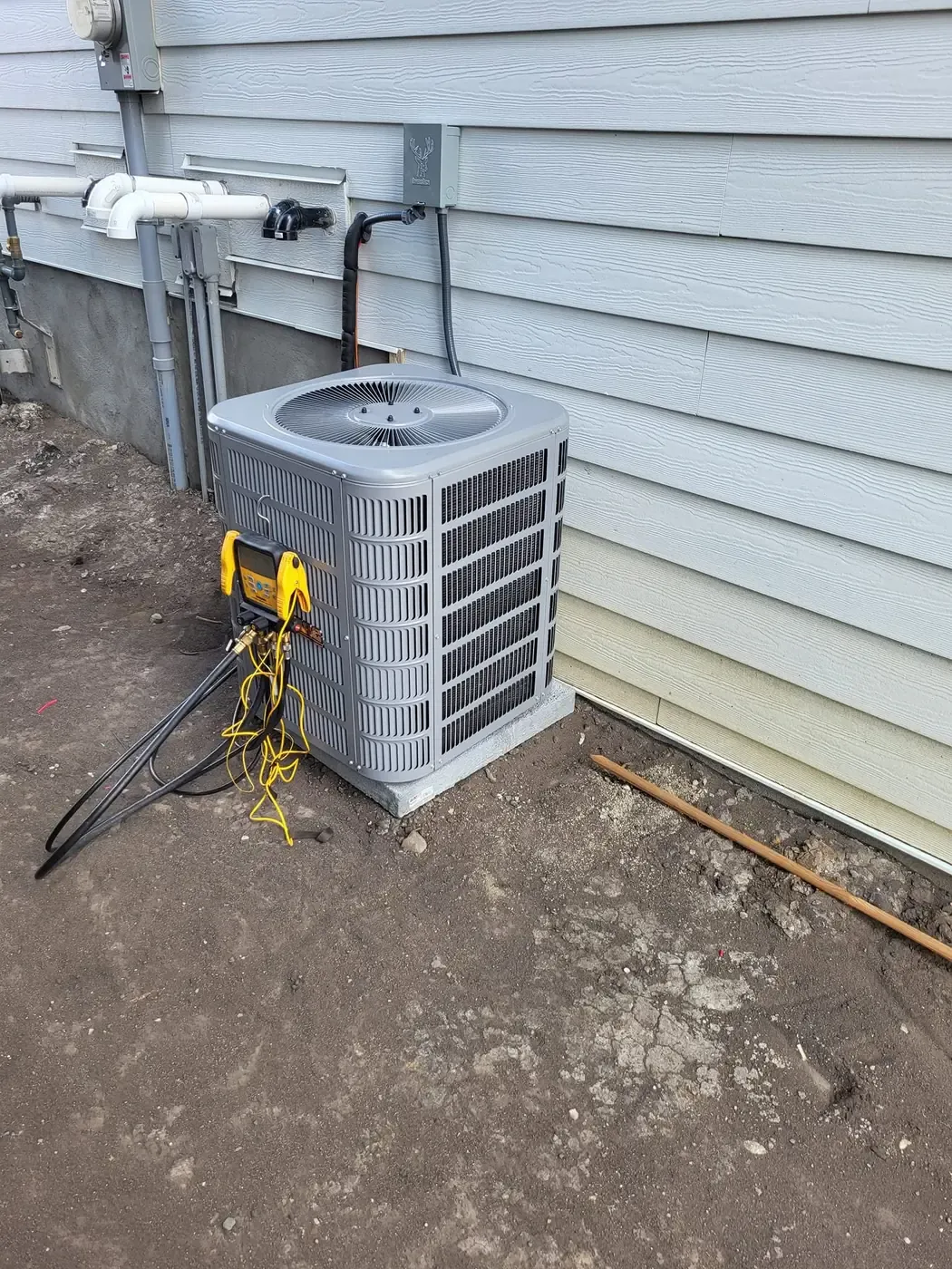 A new air conditioner on fresh soil beside grey siding, with service gauges hooked up