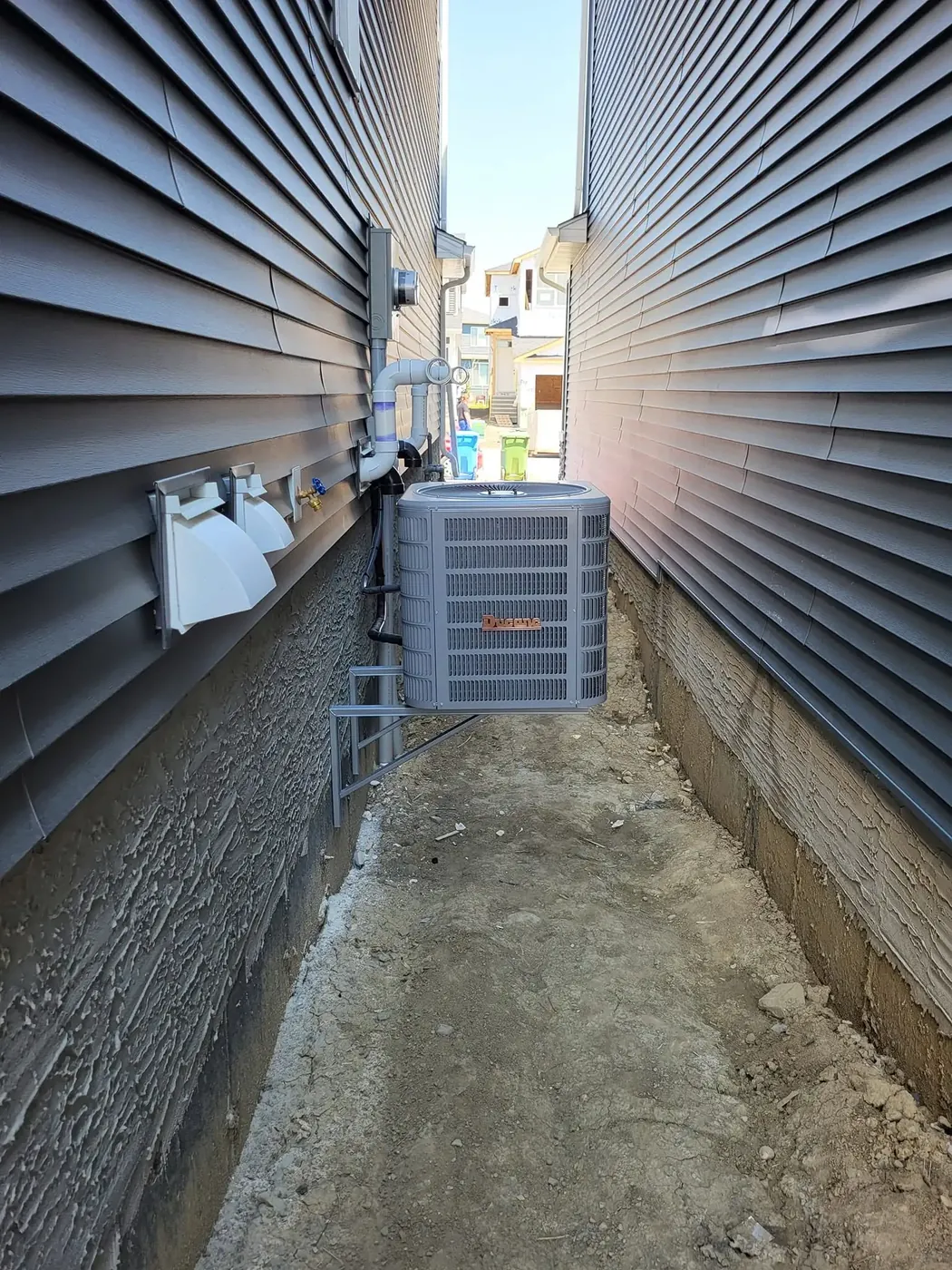 A central air conditioner on its pad in a narrow side yard between two houses