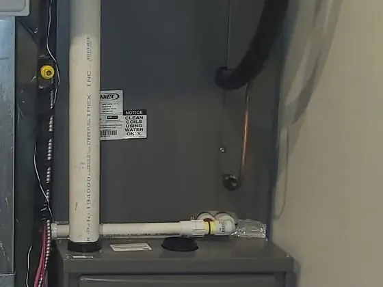 A dark grey high-efficiency furnace with white PVC venting in a narrow utility space