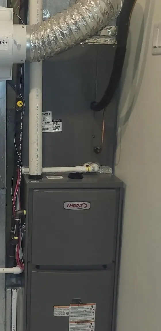 A dark grey high-efficiency furnace with white PVC venting in a narrow utility space