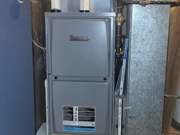 A grey high-efficiency furnace installed in a utility room beside its ductwork