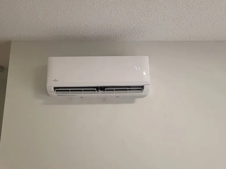 A ductless mini-split head mounted high on a white wall